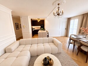 A modern living room with a sectional sofa, a dining area with a round table, and a kitchen in the background. - NEW - Haussmann-Style Appartment - 6 Guests - Disney & shopping (Serris)