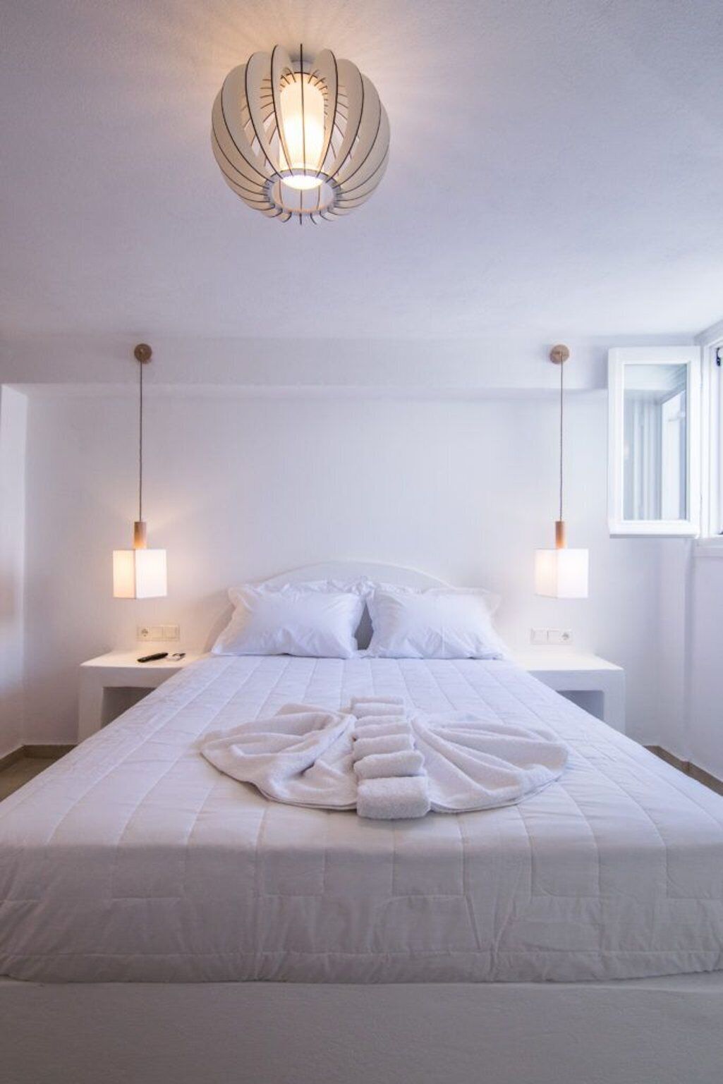 Habitación de hotel con una cama grande, dos mesitas de noche, una lámpara fijada a la pared y una ventana.