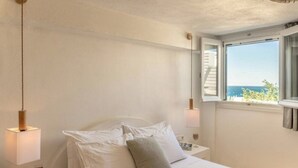 A bedroom with a bed, bedside lamps, a window with a view, and a wall-mounted light fixture. - Virelian Studio, Divine Sea Views, Furnished Terrace, Naxos (Plaka)