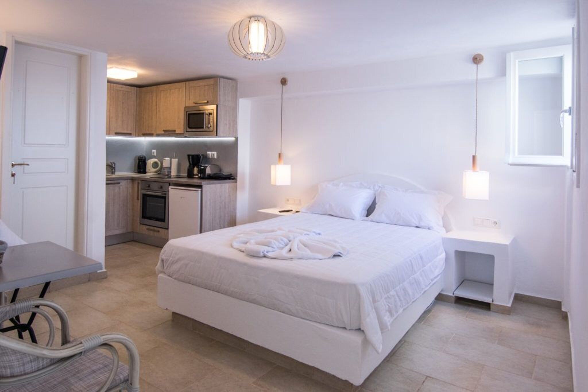 A hotel room with a bed, bedside tables, a desk, a kitchenette, and a bathroom.