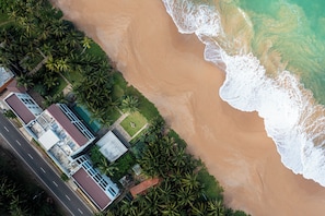 An aerial view of a coastal property with a beachfront, a road, and a building with multiple rooms.