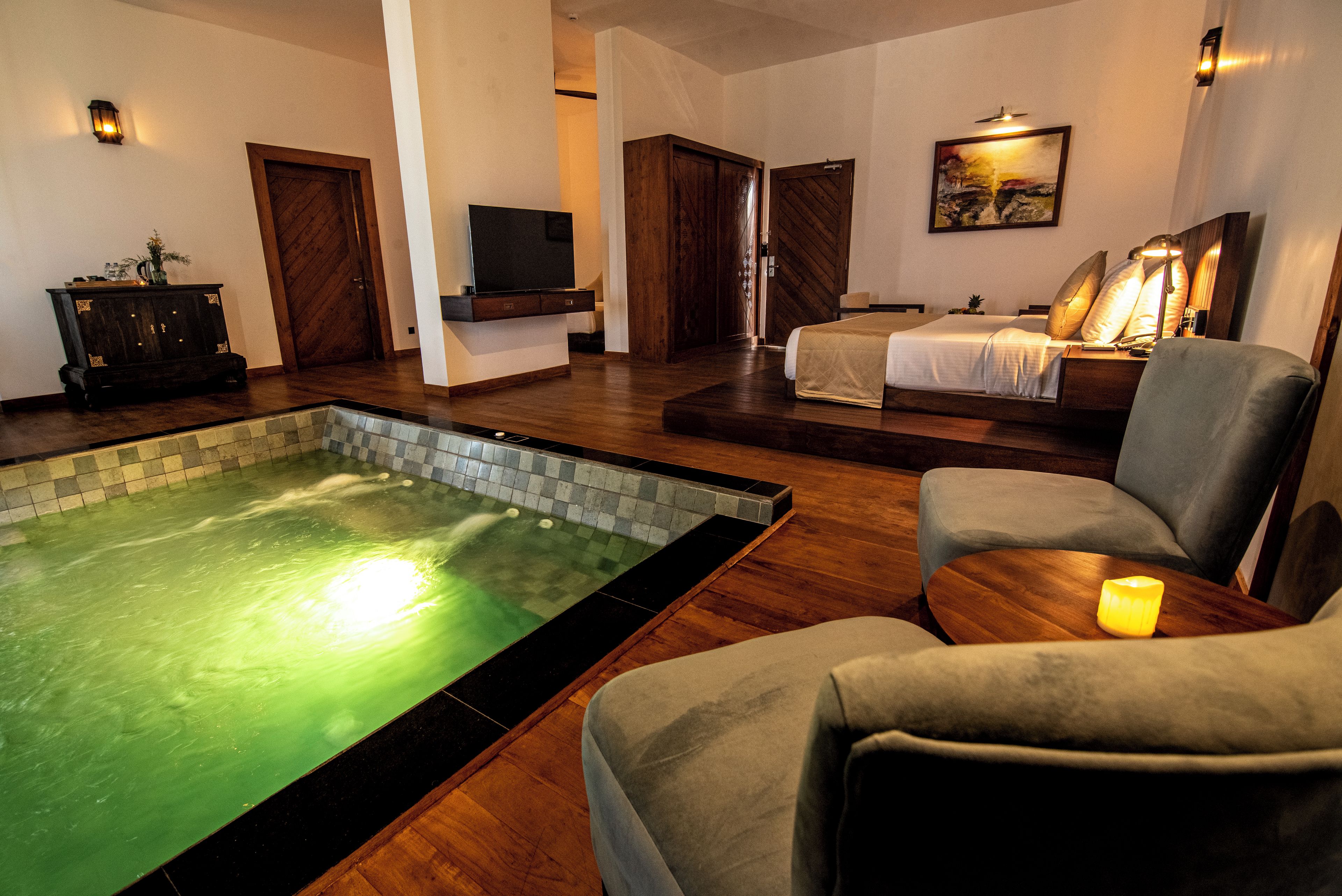 A hotel room with a spa area, including a hot tub, a bed, and a seating area with a lamp.