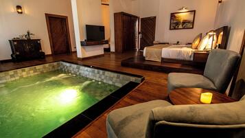 A hotel room with a spa area, including a hot tub, a bed, and a seating area with a lamp.