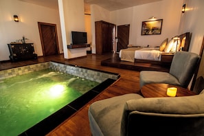 A hotel room with a spa area, including a hot tub, a bed, and a seating area with a lamp.