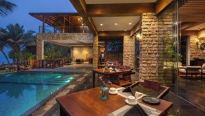 A poolside dining area with a stone wall, wooden furniture, and a view of the pool. - The Rockwall Boutique Hotel (Maha Induruwa)