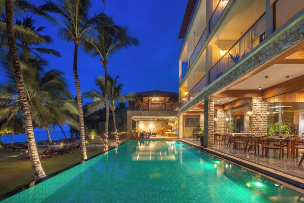 A poolside area with a clear pool, palm trees, and a building with a stone facade.