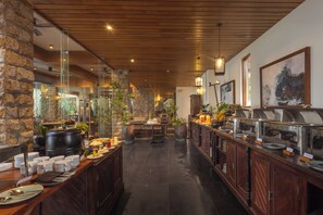 A restaurant with a buffet setup, stone walls, wooden ceiling, and indoor plants.