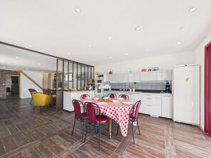 A modern kitchen with white cabinets, a dining area with a red and white checkered tablecloth, and a yellow chair. - Family house for 8 – garden & BBQ (Longeville-sur-Mer)