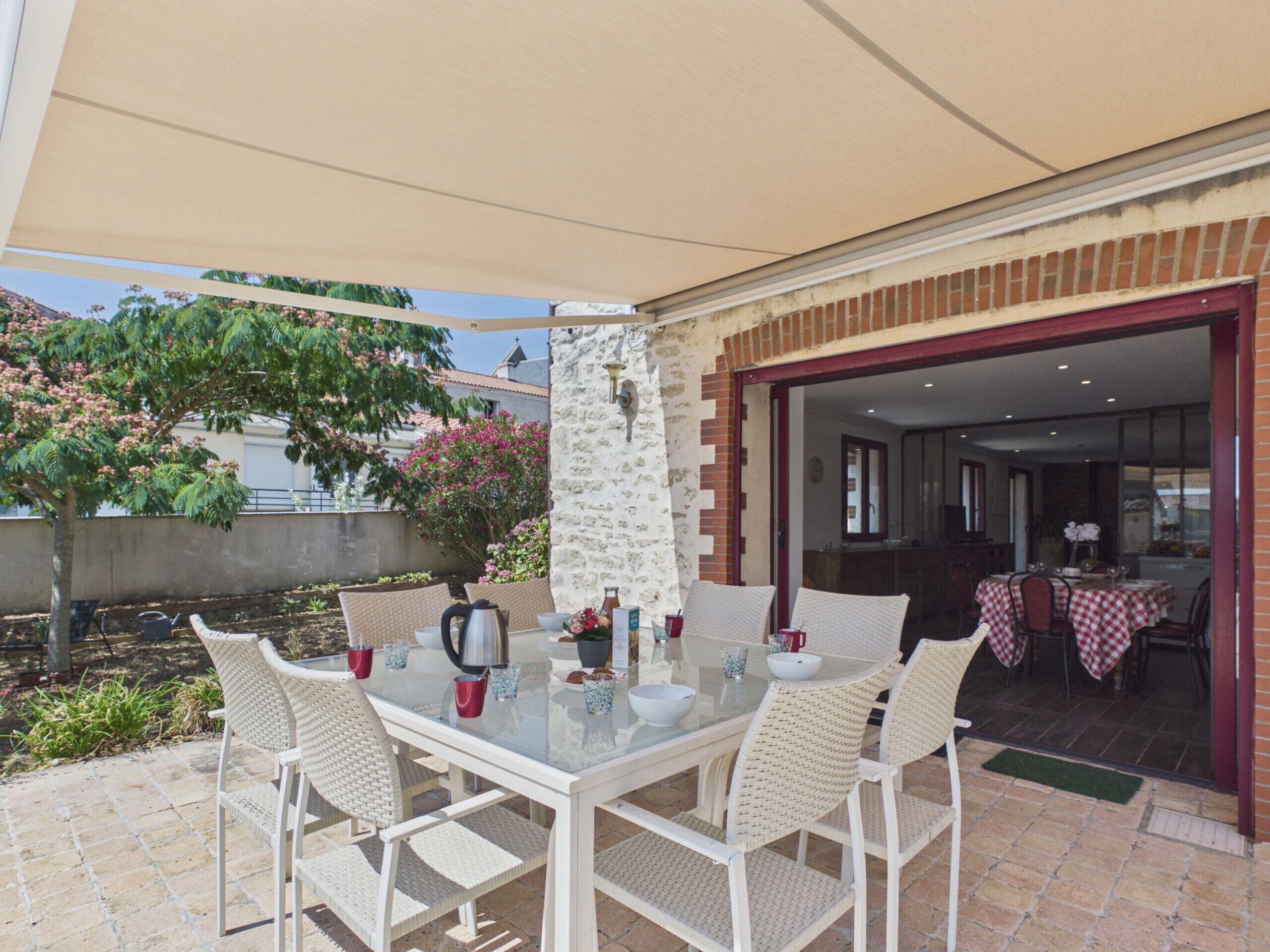 An outdoor patio with a glass table, white wicker chairs, and a stone wall.