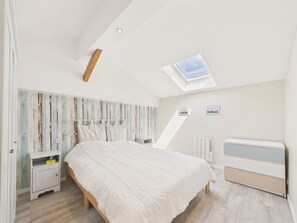 A bedroom with a sloped ceiling, a skylight, a bed, a nightstand, a bedside table, and a radiator. - Family house for 8 – garden & BBQ (Longeville-sur-Mer)