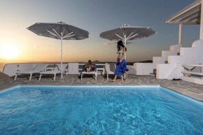Ein Poolbereich mit Liegestühlen und Sonnenschirmen, ein klarer Himmel und ein Sonnenuntergang.