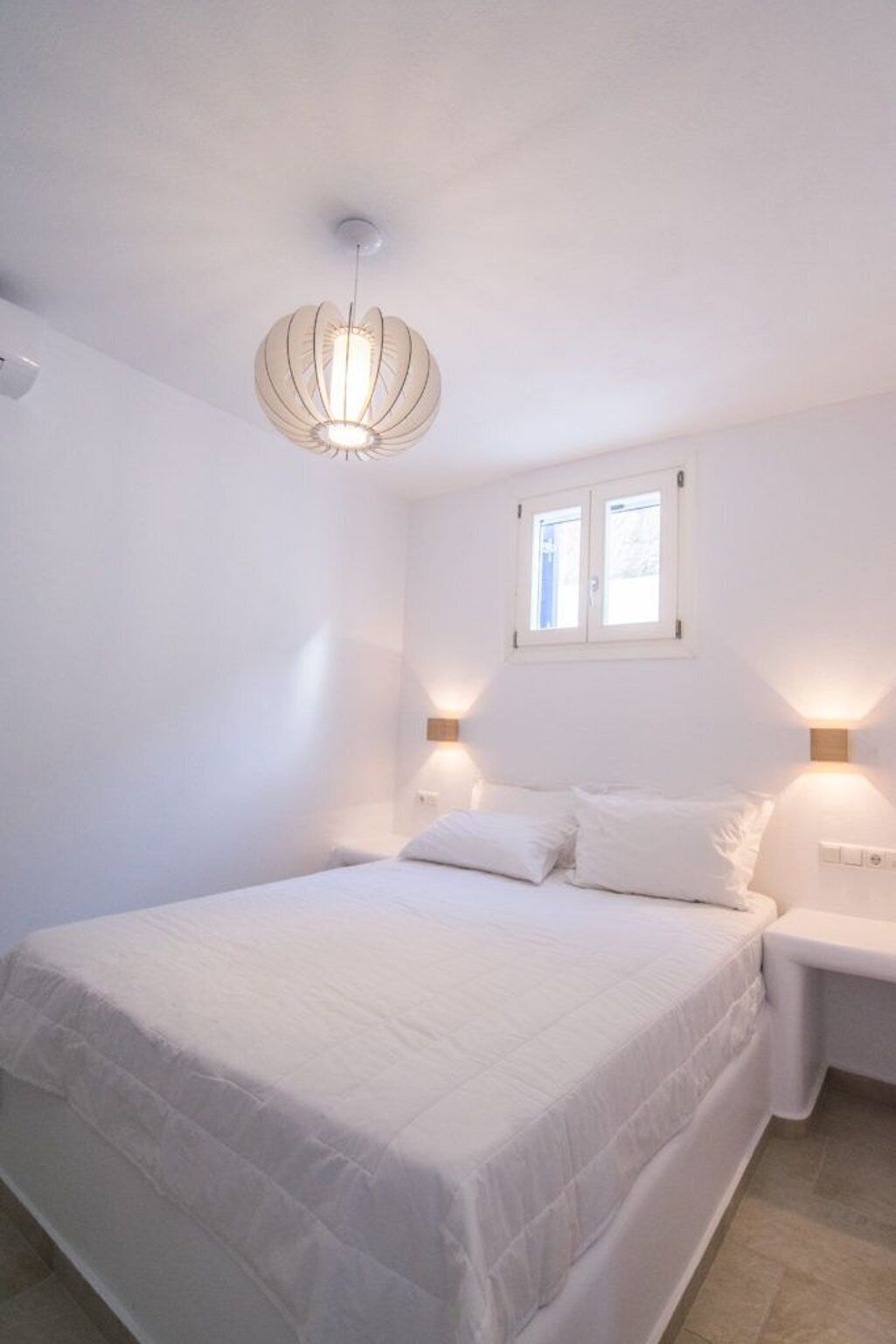A bedroom with a large bed, a ceiling light fixture, two bedside lamps, and a window.