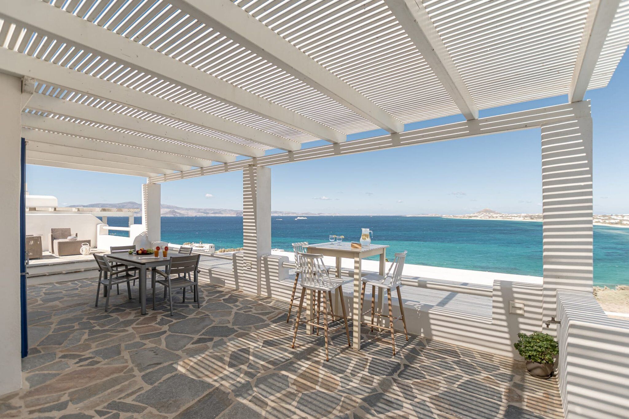 A covered outdoor seating area with a table and chairs, overlooking a coastal view.