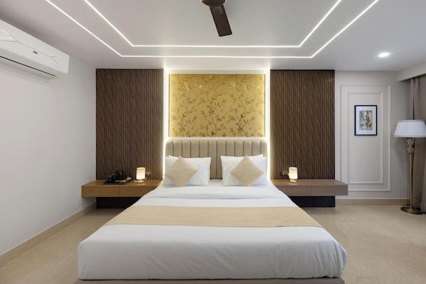 A modern hotel room with a large bed, bedside tables, a ceiling fan, and a wall-mounted air conditioner. - SERENEWOOD BY ZENVANA (Dehradun)