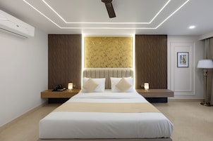 A modern hotel room with a large bed, bedside tables, a ceiling fan, and a wall-mounted air conditioner.