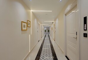 A hotel hallway with a patterned floor, framed artwork on the walls, and doors numbered 306. - SERENEWOOD BY ZENVANA (Dehradun)