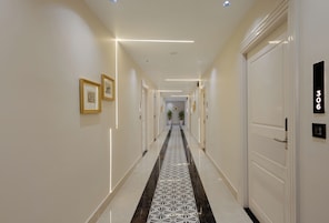 Un corridoio d'hotel con pavimento decorato, opere d'arte incorniciate alle pareti e porte numerate 306.