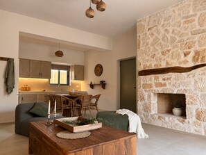 A modern living room with a stone fireplace, a dining area with a wooden table and chairs, and a kitchen with wooden cabinets and a window. - Conte Maris Tower III - Sea View Mediterranean Escape (Tragaki)