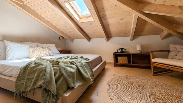 A bedroom with a sloped ceiling, a skylight, a bed, a bedside table, a chair, and a woven rug. - Conte Maris Tower III - Sea View Mediterranean Escape (Tragaki)