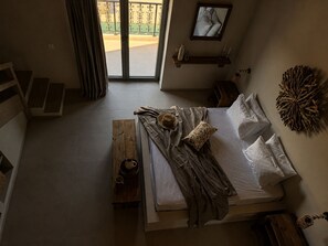 Ein Schlafzimmer mit einem Bett, einem Holznachttisch, einer Bank und Blick ins Freie.