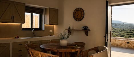 A spacious kitchen with wooden cabinets, a round dining table, wicker chairs, and a view through an open door.