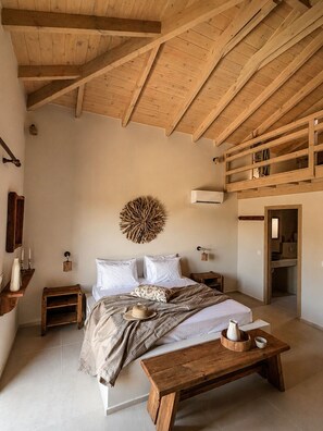 A bedroom with a wooden ceiling, a bed with white linens, a wooden bench, and a wall-mounted decorative piece. - Conte Maris Tower III - Sea View Mediterranean Escape (Tragaki)