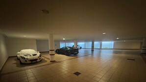 A spacious indoor parking area with tiled floors and two cars parked. - Ca dei Nani - Exclusive Stay with Sauna (Cortina d'Ampezzo)