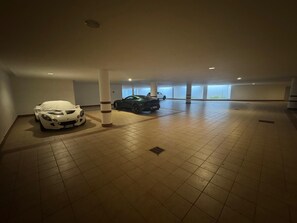 Ett rymligt, inomhusbeläget parkeringsområde med kaklade golv och två parkerade bilar.