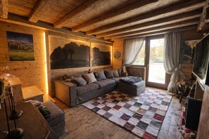 A cozy room with a sofa, a quilted rug, wooden walls, and a clock. - Ca dei Nani - Exclusive Stay with Sauna (Cortina d'Ampezzo)