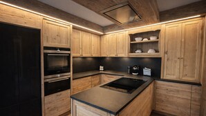 A modern kitchen with wooden cabinetry, a black refrigerator, stainless steel appliances, and a black countertop. - Ca dei Nani - Exclusive Stay with Sauna (Cortina d'Ampezzo)
