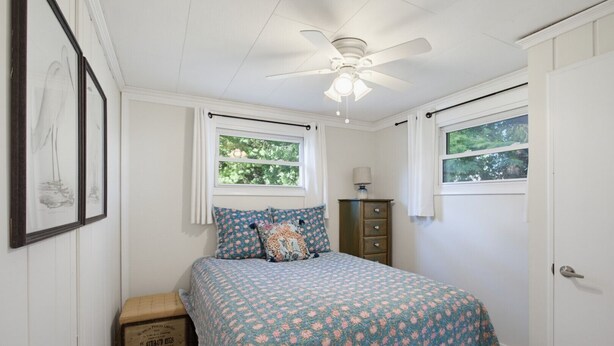 A bedroom with a bed, a ceiling fan, two windows, a dresser, and a framed picture on the wall. - The Cottage at Port Austin (Port Austin)