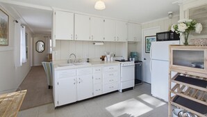 A compact kitchen with white cabinets, a sink, a stove, and a microwave. - The Cottage at Port Austin (Port Austin)