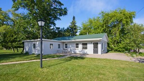 A single-story house with a green roof, a front porch, and a small attached garage. - The Cottage at Port Austin (Port Austin)