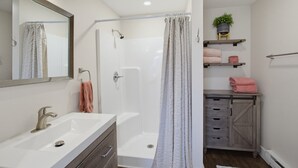 A modern bathroom with a shower, a sink, a mirror, and a wooden cabinet. - The Cottage at Port Austin (Port Austin)