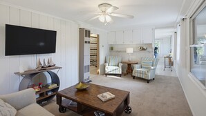 A living room with a flat-screen TV, a wooden coffee table, striped armchairs, and a ceiling fan. - The Cottage at Port Austin (Port Austin)