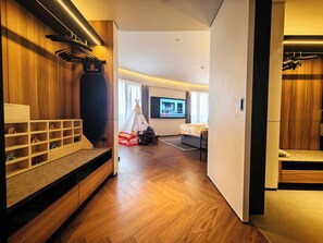Quarto de hotel moderno com piso de madeira, uma cama, televisão, guarda-roupa e um espaço de brincadeira com brinquedos e uma tenda.