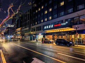 Un hôtel doté d’une façade moderne, d’une entrée bien visible et d’un parking où sont garées des voitures.