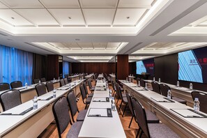 Ein Konferenzraum mit langen Tischen, Stühlen und einem großen Bildschirm, der Text zeigt.