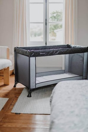A room with a crib, a window with curtains, a floor lamp, and a white rug.