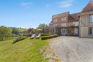 Une grande maison en briques avec une allée en gravier et une pelouse agrémentée de deux chaises longues.