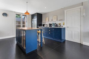 A modern kitchen with dark flooring, a blue island, and a white door.