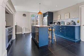 A modern kitchen with dark flooring, a central island, bar stools, and a built-in oven.