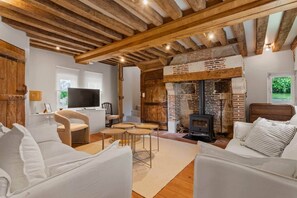 A rustic interior with exposed wooden beams, a brick fireplace, and a cozy seating area with white sofas.
