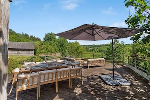 An outdoor dining area with a wooden deck, a table set for four, and a large umbrella providing shade.