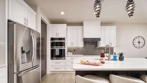 Una cocina moderna con armarios blancos, electrodomésticos de acero inoxidable, salpicadero tipo espiga y una isla central con taburetes de bar.