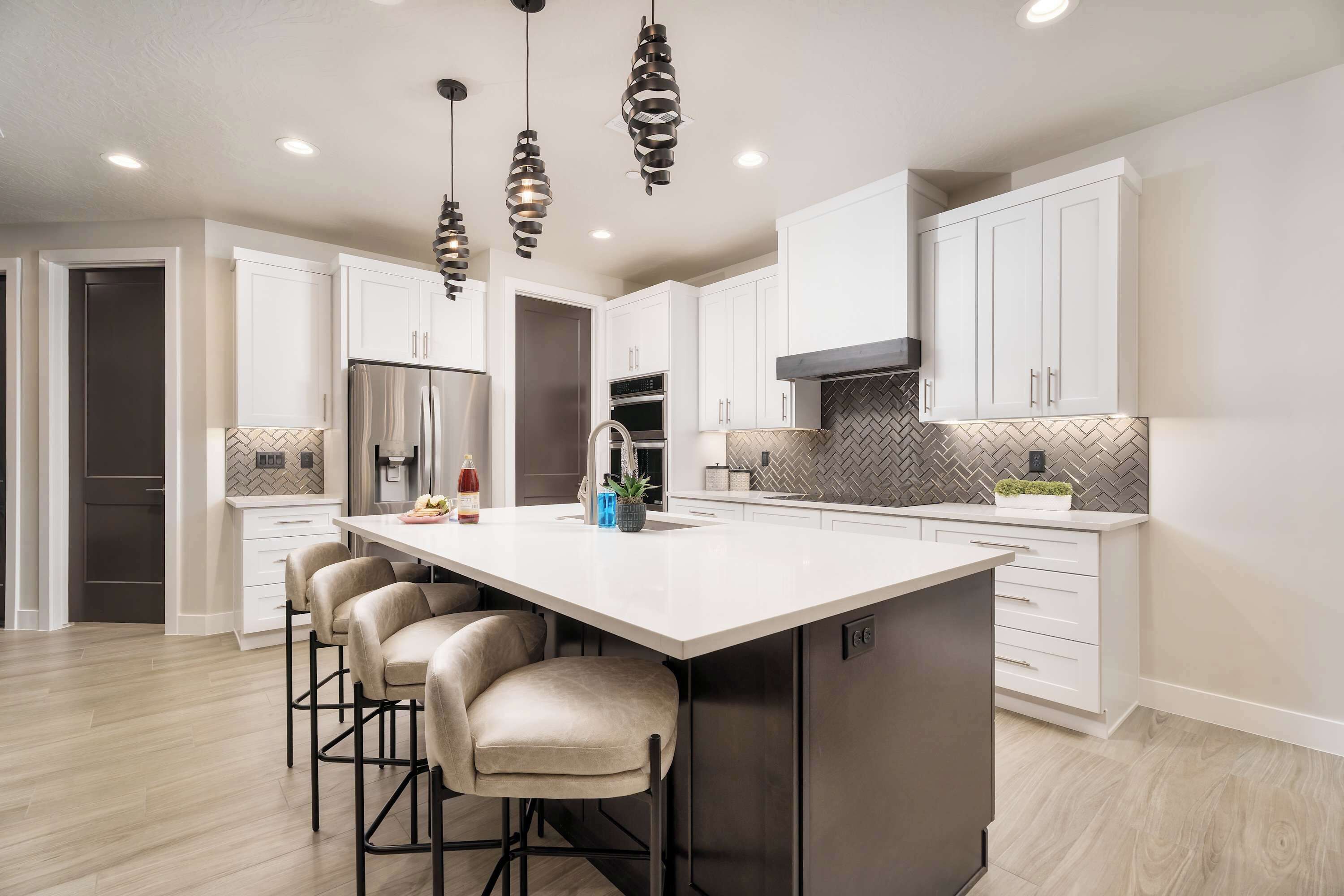 A modern kitchen with white cabinets, a large island with bar stools, stainless steel appliances, and pendant lighting.