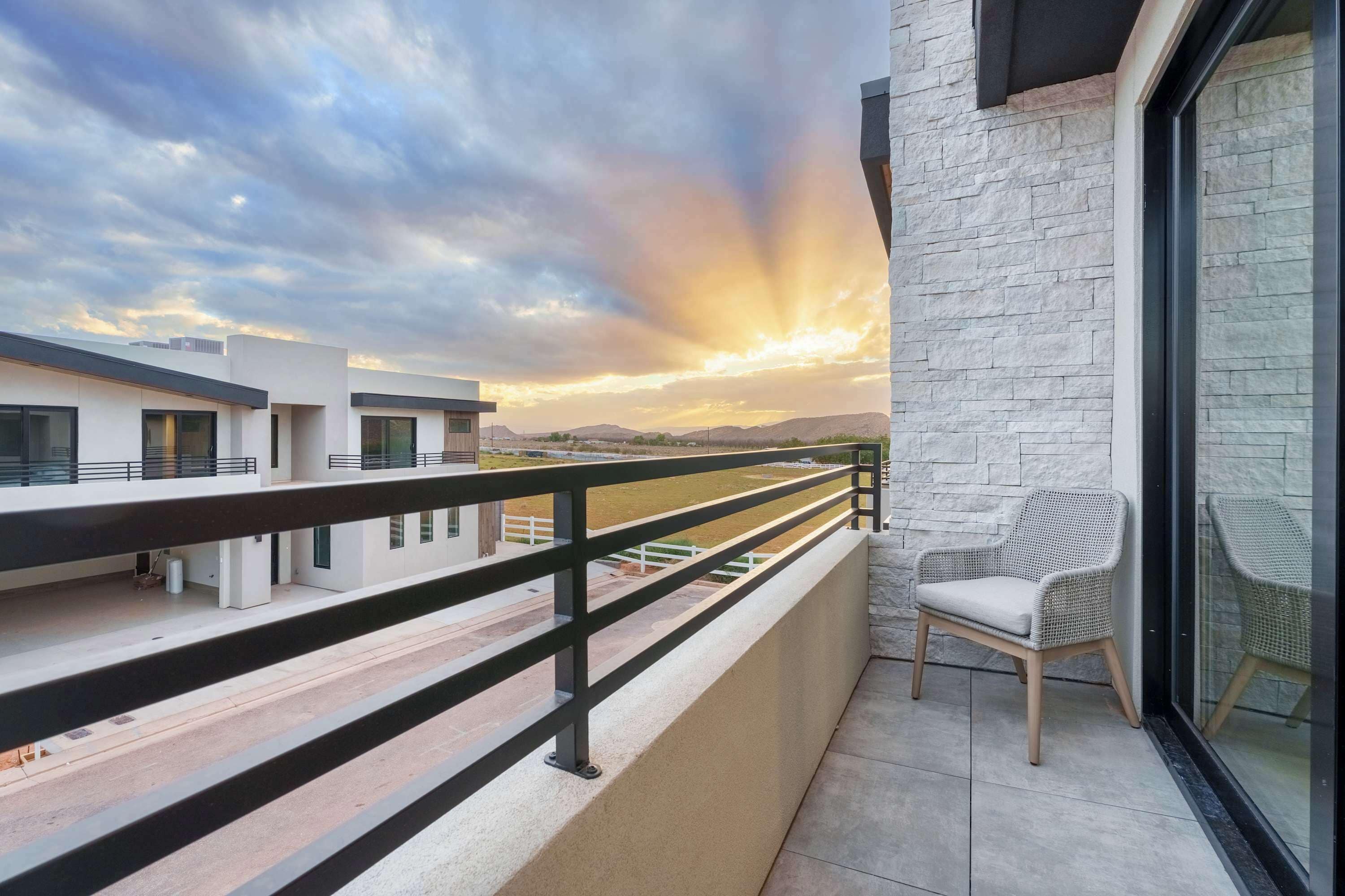 Ein Balkon mit Blick auf einen Sonnenuntergang über einer Berglandschaft, ein Korbstuhl und eine Steinmauer.