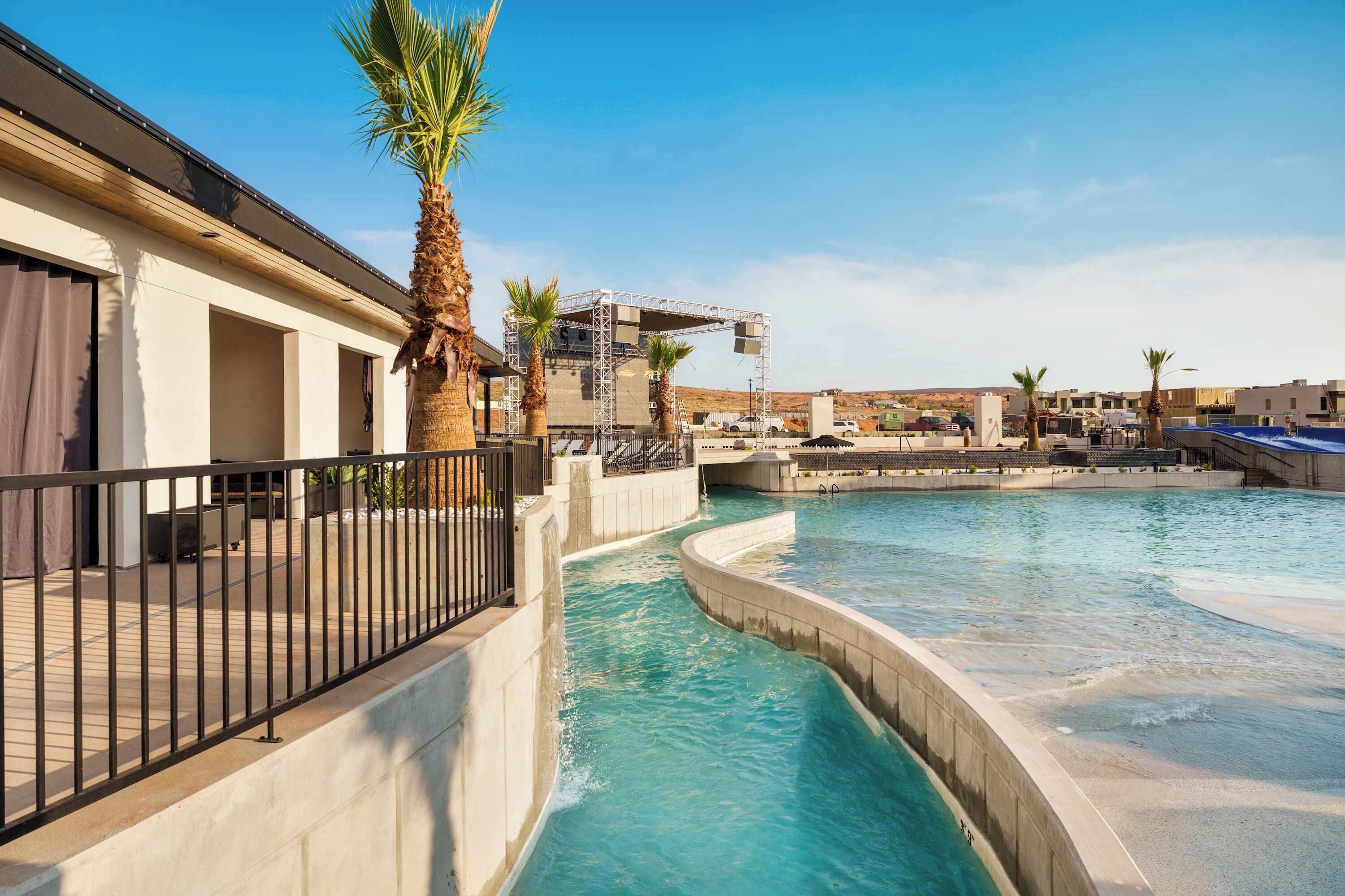 A swimming pool with a curved design, a palm tree, and a stage structure in the background.
