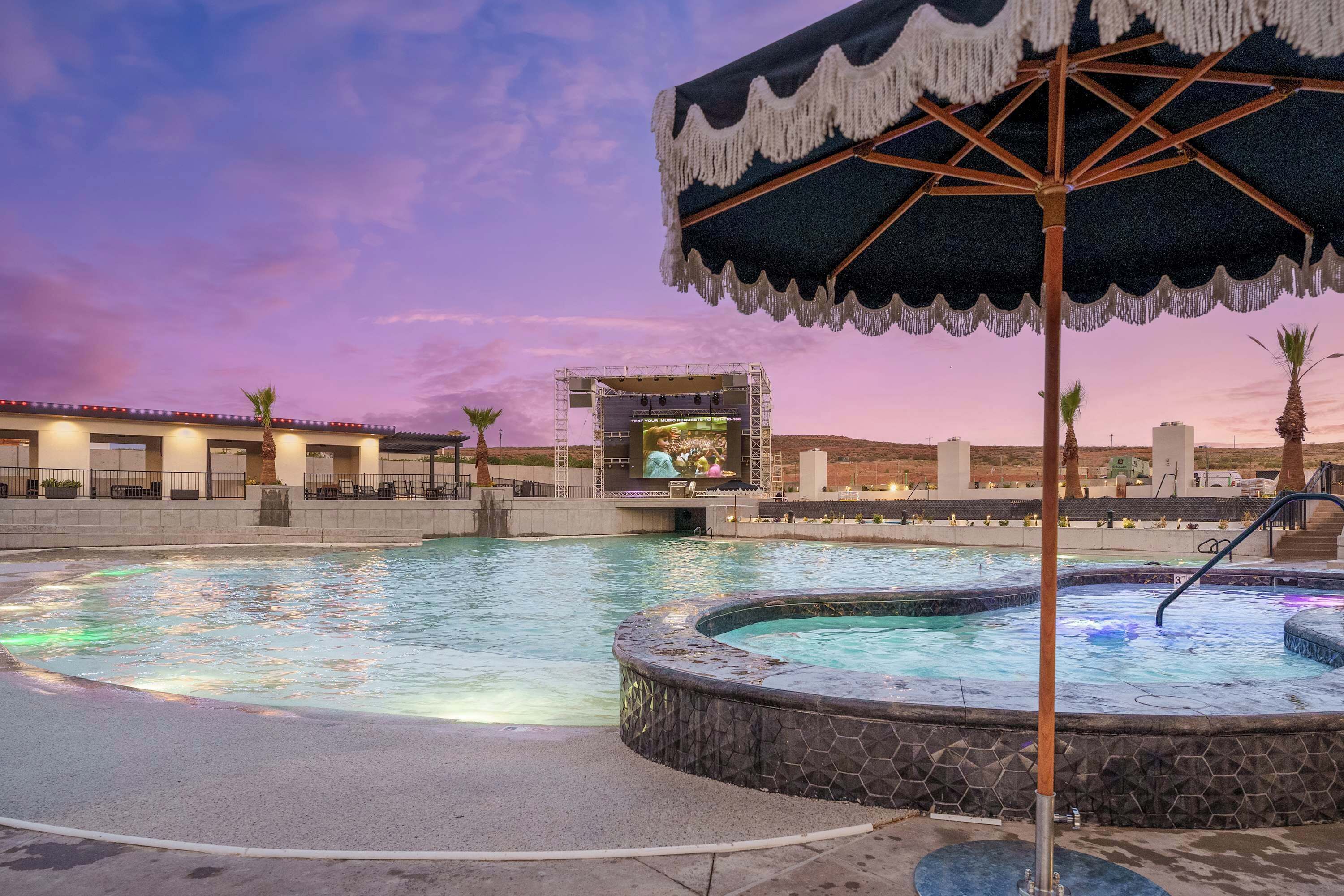 A swimming pool with a hot tub, a stage, and an umbrella.