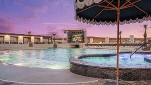 Una piscina con hidromasaje, un escenario y una sombrilla.